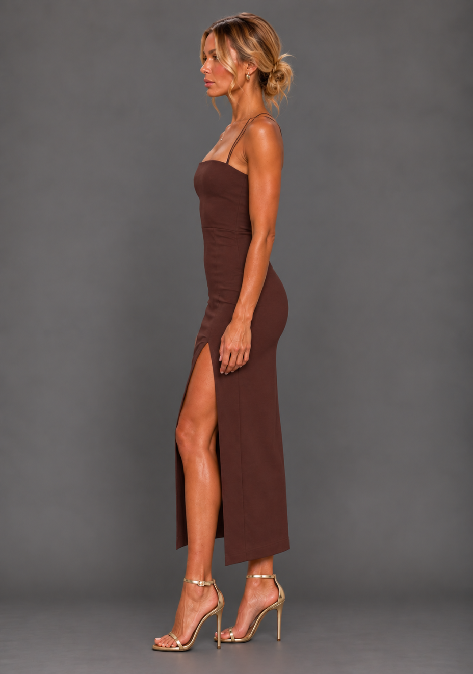 Side front image of a model wearing the VSPR Alyssa Chocolate Midaxi Dress, showcasing the sleek body-skimming fit and elegant front skirt split against a grey studio backdrop.