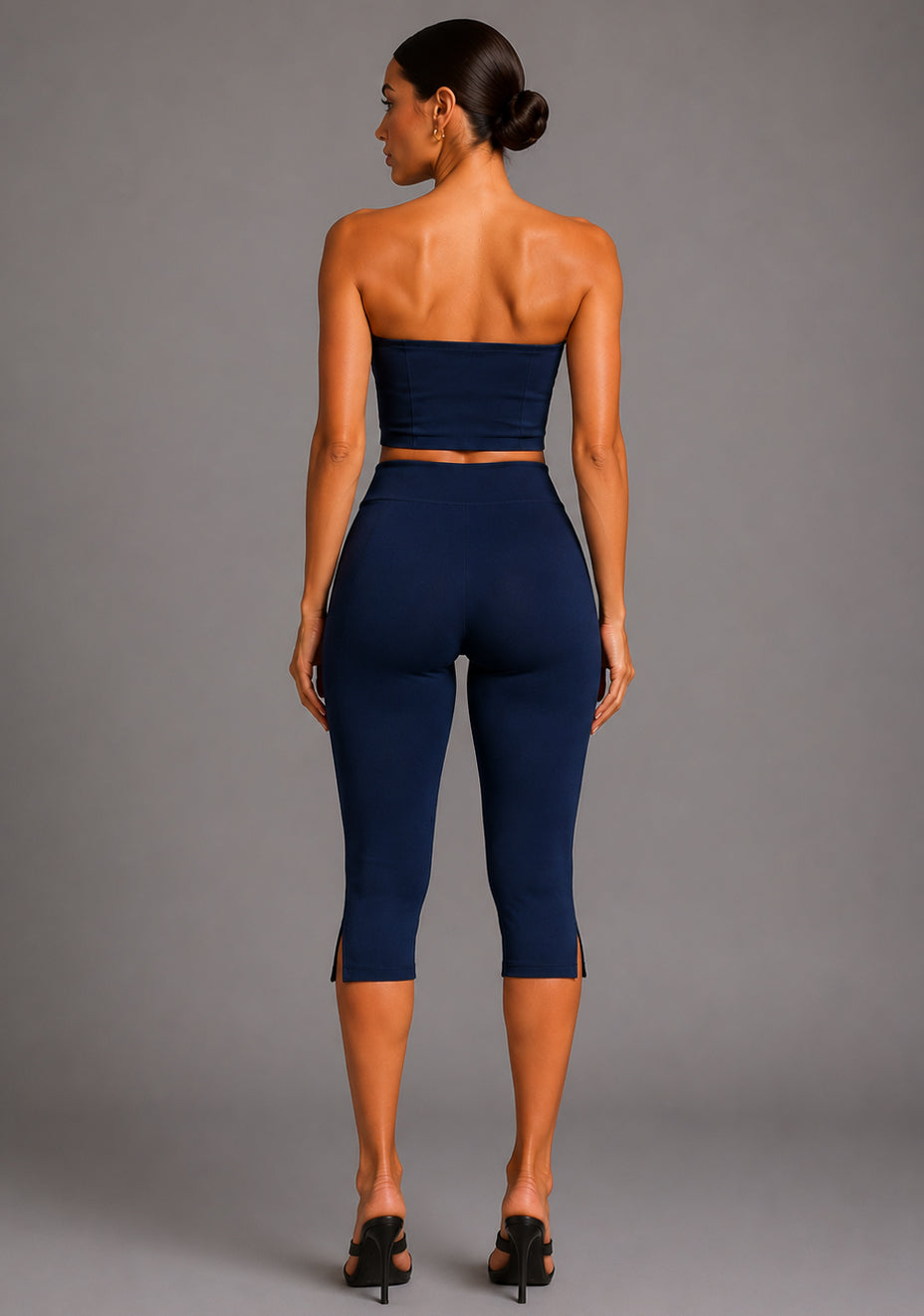 Back image of a model wearing the VSPR Benedetta Strapless Navy Crop Top with Capri Navy Trousers in navy, featuring a clean strapless back, figure-enhancing fit, and high-waisted tailored trousers against a grey studio backdrop.