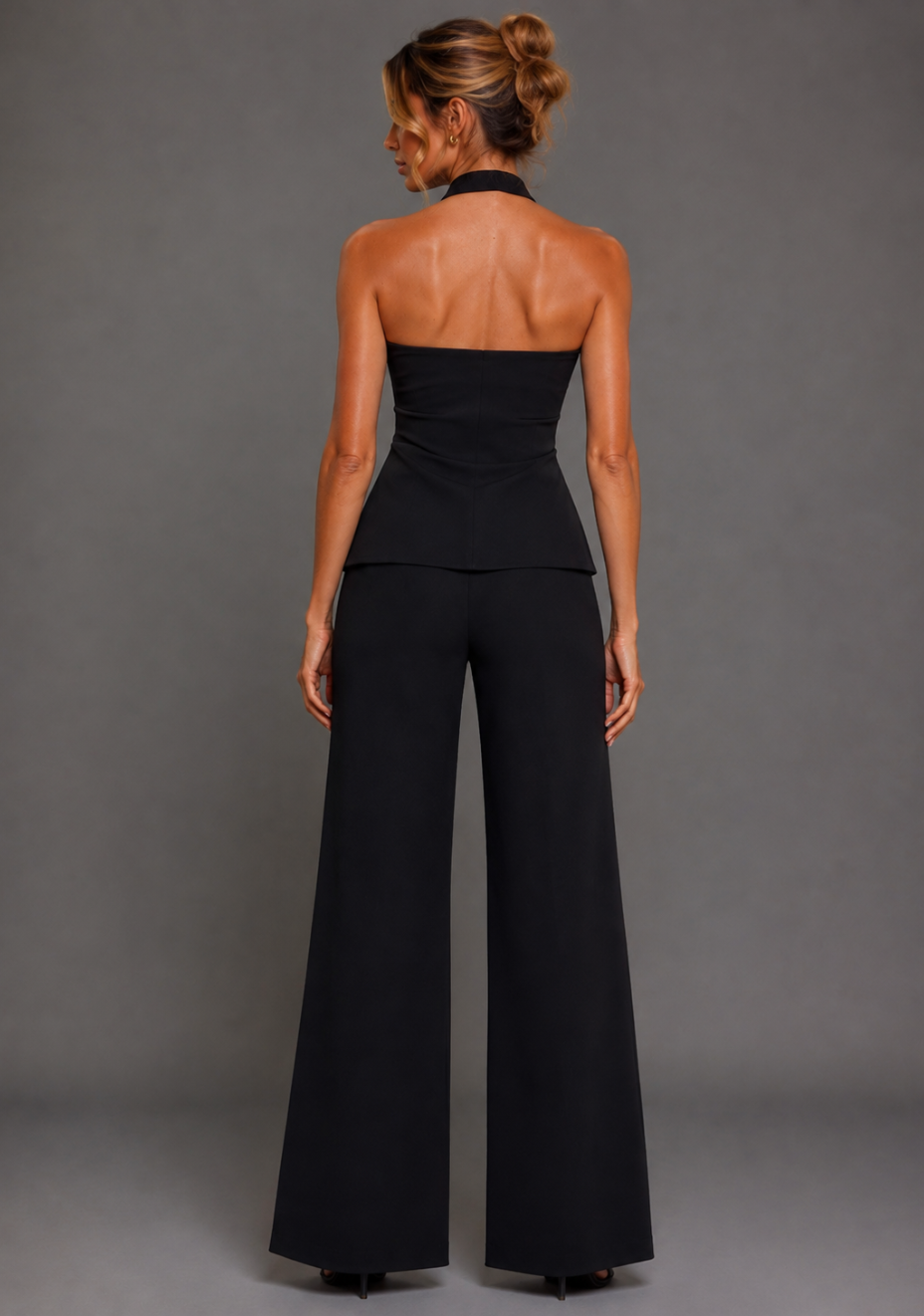 Back image of a model wearing the VSPR Betty Tailored Longline Black Waistcoat with Elton Wide Leg Black Tailored Trousers, showcasing the elongated silhouette and clean tailoring against a grey studio backdrop