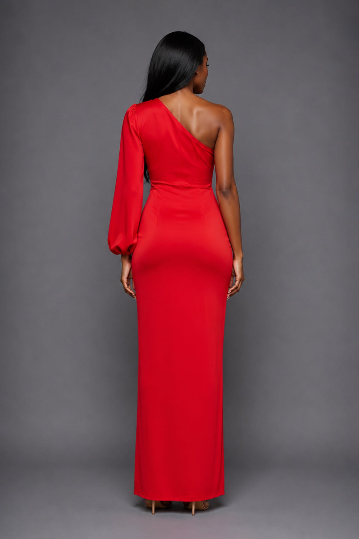 Back image of a model wearing the VSPR Keaton One Sleeve Red Maxi Dress, showcasing its elegant floor-length silhouette and refined drape against a grey studio backdrop.