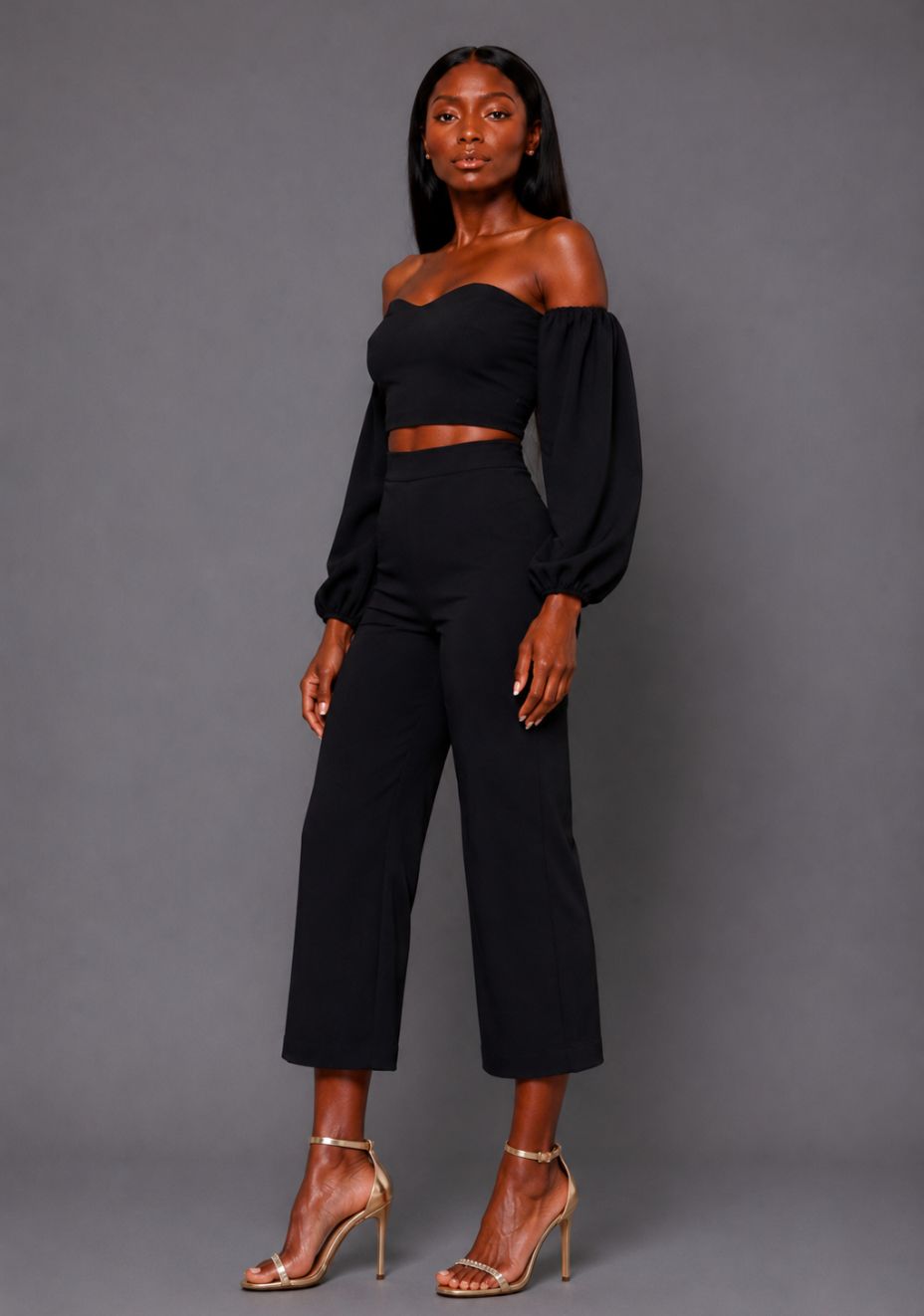 Side front image of a model wearing the VSPR Mindi Wide Leg Black Cropped Trousers, highlighting the high-rise fit and fluid wide-leg silhouette against a grey studio backdrop.