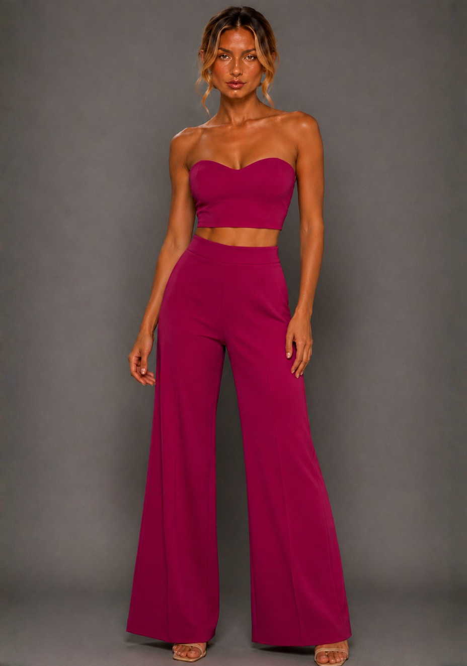 Front image of a model wearing the VSPR Marty Magenta Wide Leg Pants with a high-rise waist and sweeping wide-leg silhouette, styled with the matching VSPR Renata Strapless Magenta Crop Top, standing straight-on against a grey studio backdrop.