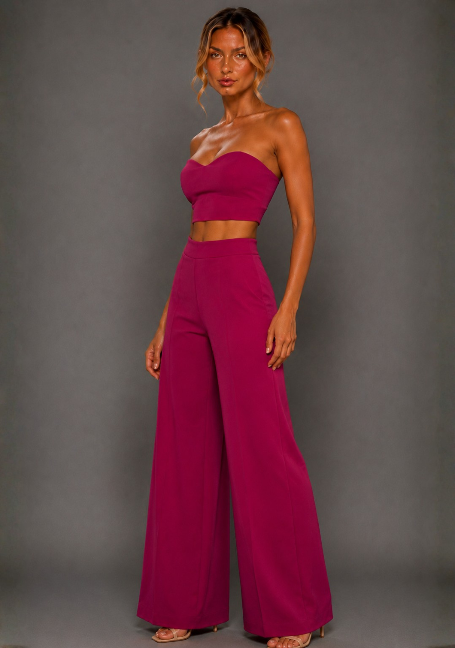 Front image of a model wearing the VSPR Marty Magenta Wide Leg Pants with a high-rise waist and sweeping wide leg, paired with the matching VSPR Renata Strapless Magenta Crop Top, standing against a grey studio backdrop.