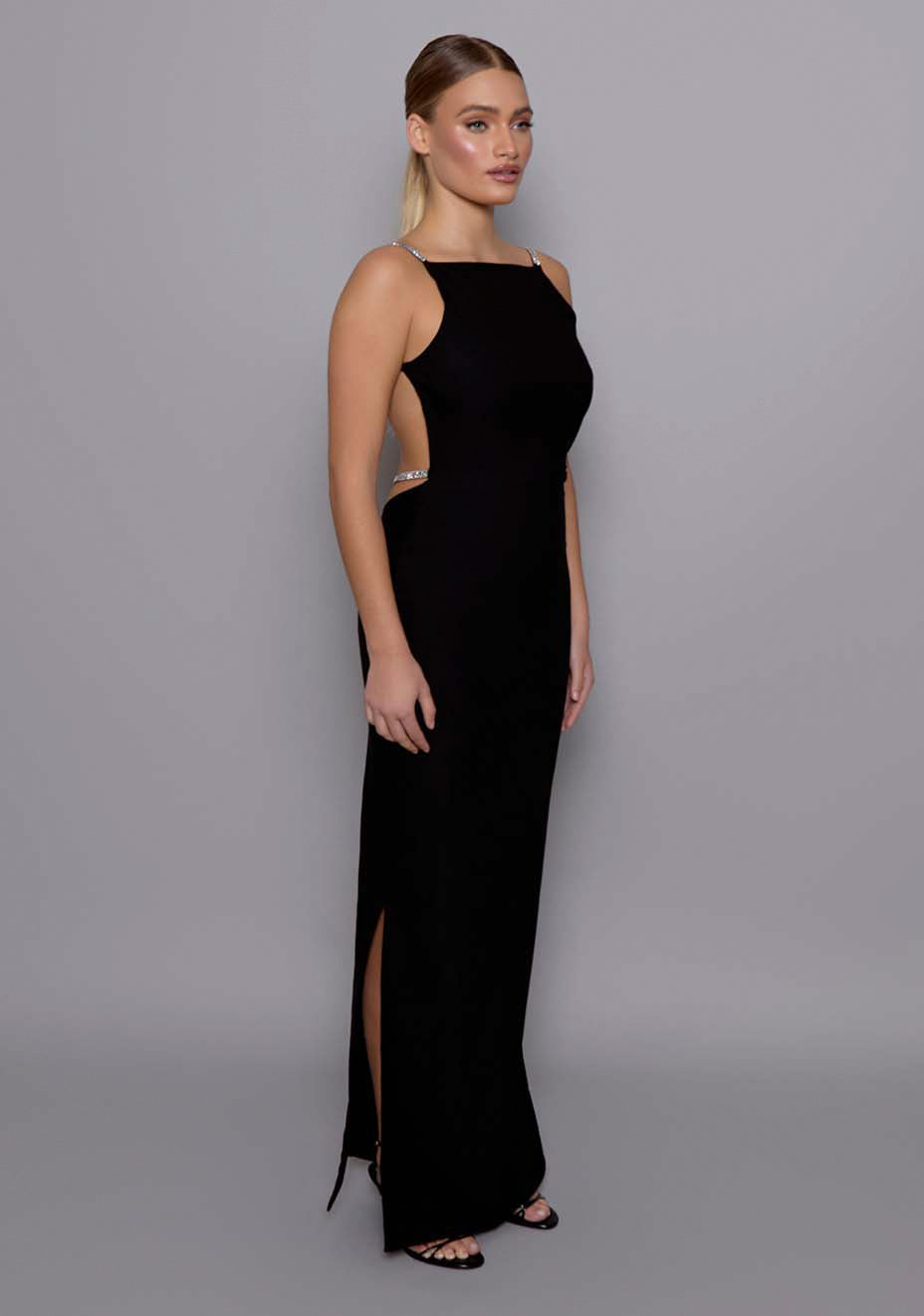 Side front image of a model wearing the VSPR Alba Open Back Maxi Dress in Black, revealing the elegant profile, square neckline, and sculpted waistline with clean, elongating lines.