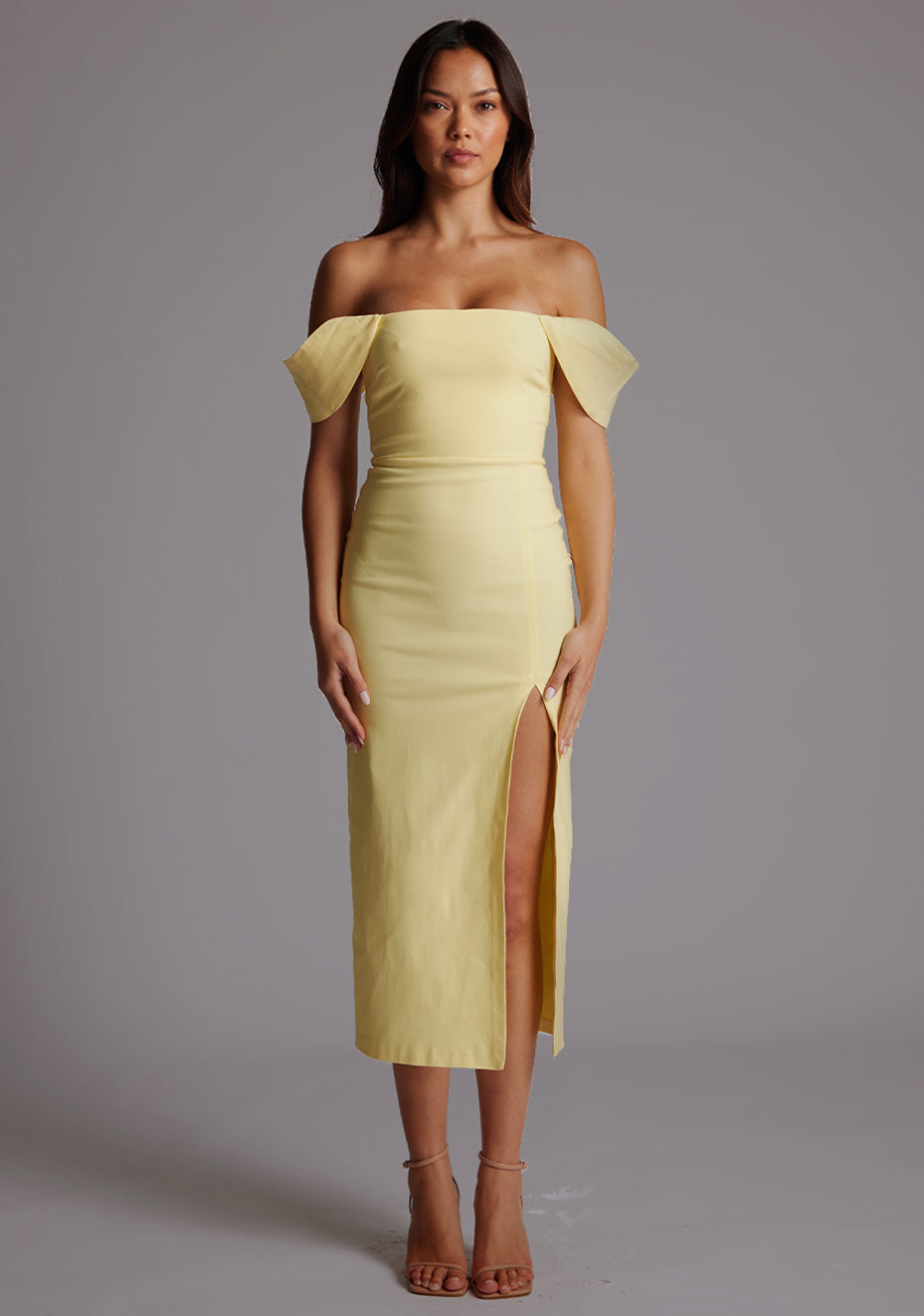 Front image of a model wearing the VSPR Astra Bardot Lemon Midaxi Dress with a Bardot neckline, fitted silhouette, and front thigh split, standing against a grey studio backdrop.
