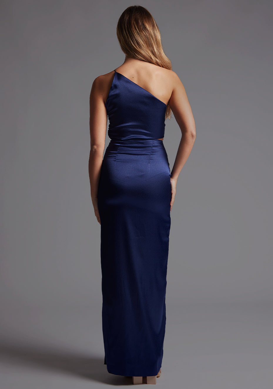 Back image of a model wearing the Vesper Esme One Shoulder Ruched Satin Maxi Dress in Navy, featuring a clean satin back and flowing maxi skirt.