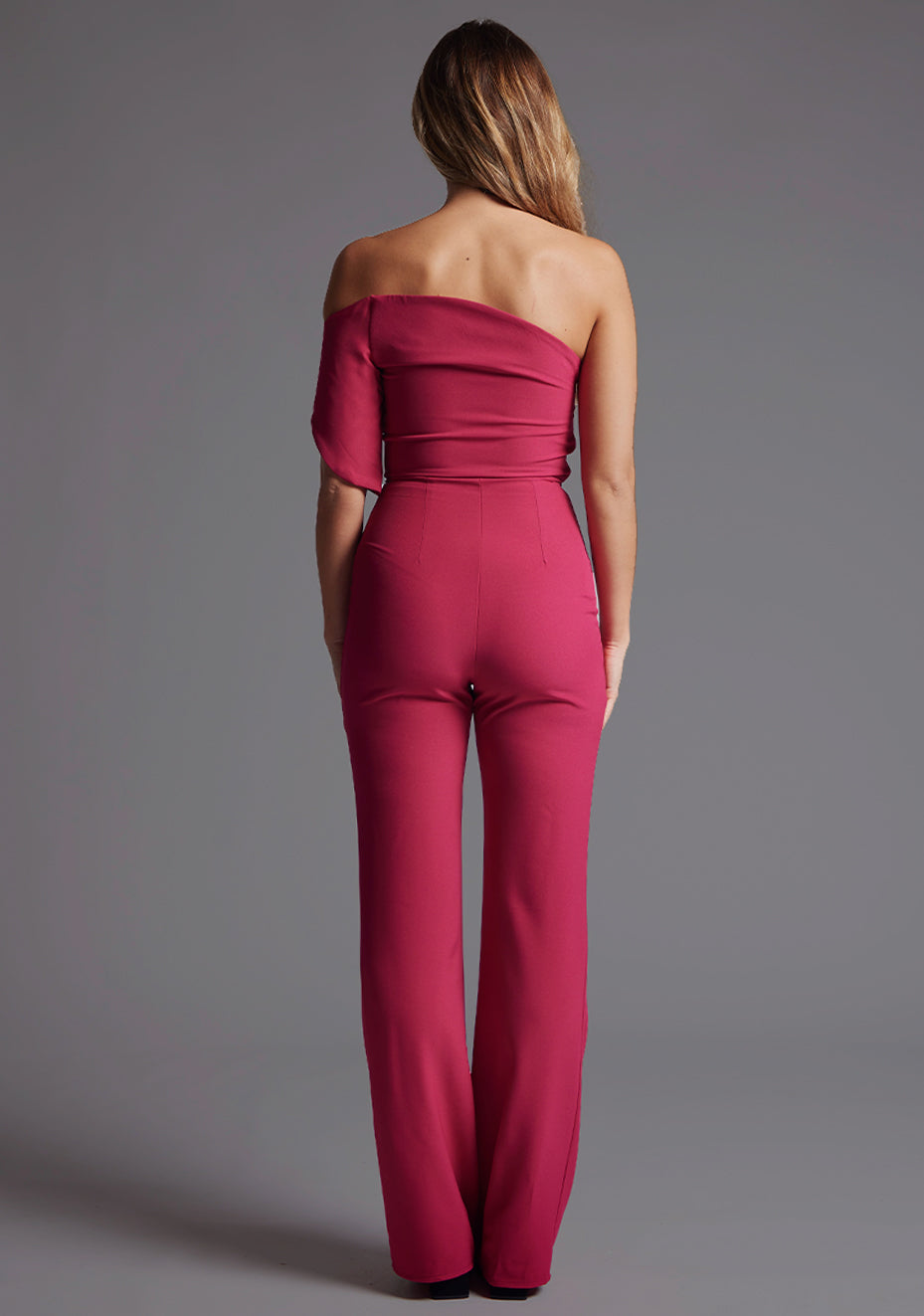 Back image of a model wearing a with a stunning one-shoulder design and a body-hugging fit that accentuates your curves in all the right places and side zip fastening ensures a seamless look. The design featured is the Vesper Ines One Shoulder Jumpsuit in Raspberry.