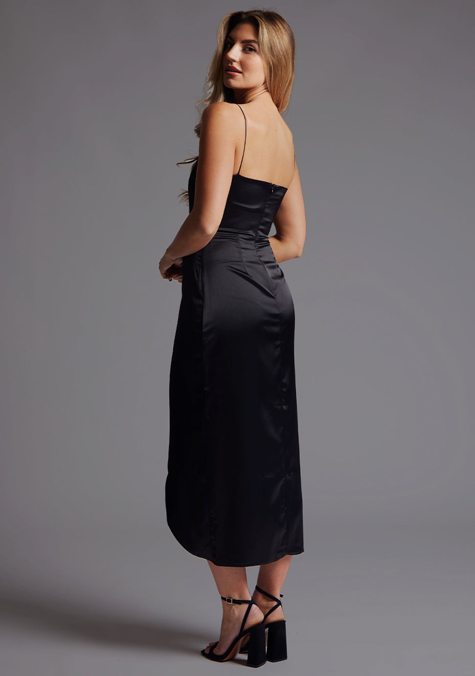 Side back image of a model wearing the Vesper Margiela Plunge Neckline Midaxi Dress in Black, highlighting the delicate straps and flowing faux wrap skirt.