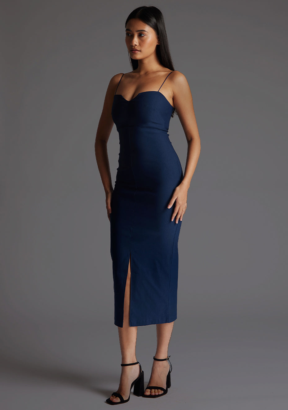 Side front image of model wearing a navy strappy midaxi dress with a sweetheart neckline, thin straps, centre front skirt split and centre back zip for a perfect fit. The design featured is the Vesper Miren Strappy Bodycon Midaxi Dress in Navy.