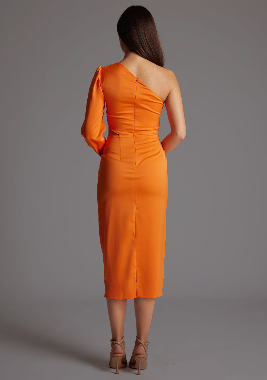 Back image of a model wearing an orange mid dress with a asymmetric, one long sleeve design and subtle side cut-out. The design featured is the Vesper Niccola Orange Midi Dress