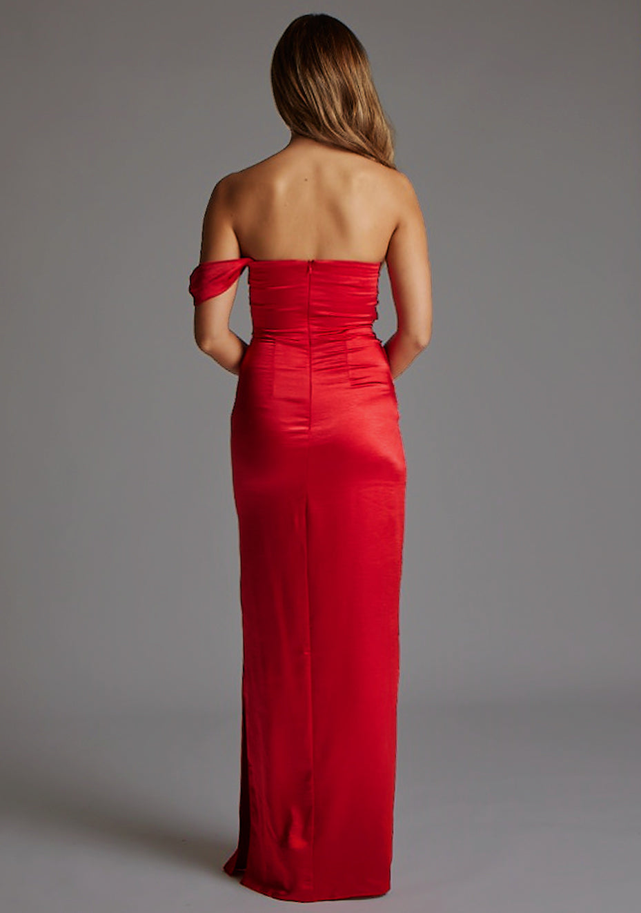 Back image of a blonde model wearing a Red Maxi Dress with a one-sleeve off-shoulder design, crafted with luxurious satin fabric, a design features Vesper Roselie Red Maxi Dress