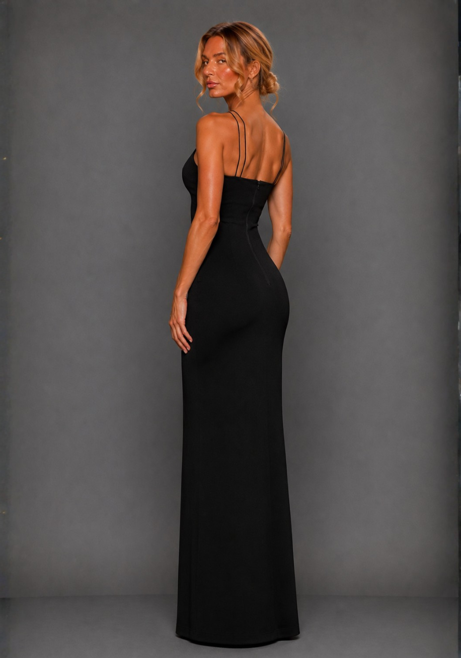Side back image of a model wearing the VSPR Auralia High Neck Strappy Black Maxi Dress, highlighting the streamlined silhouette and fitted shape against a grey studio backdrop.