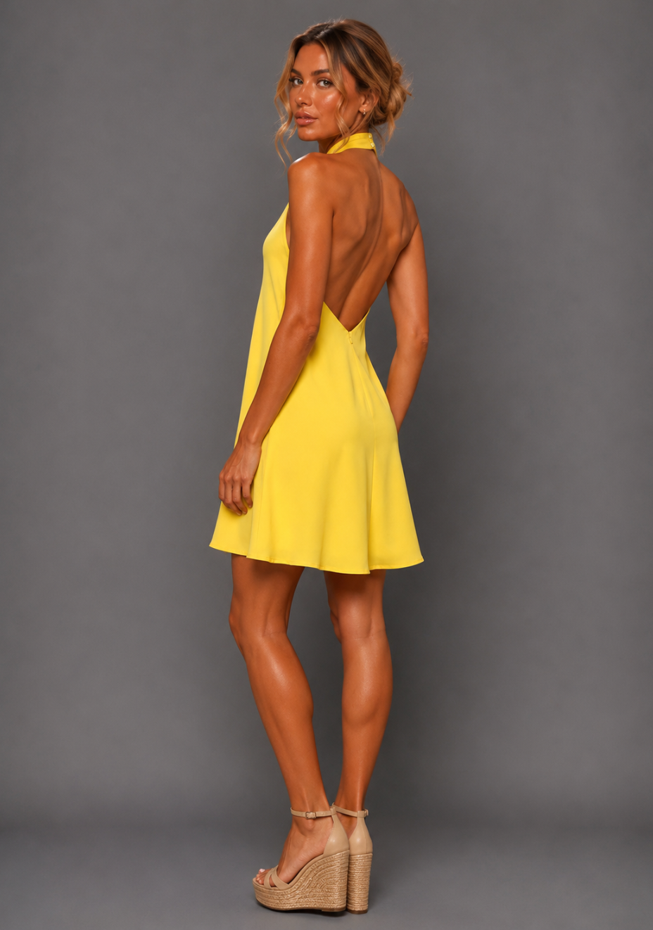 Side back image of a model wearing the VSPR Ayesha Twist Neck Yellow Mini Dress from a side back angle, revealing the elegant open V-back and relaxed flowing shape against a grey studio backdrop.
