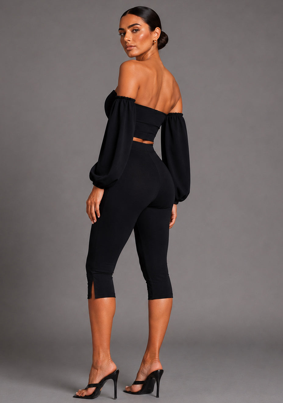 Side back image of a model wearing the VSPR Belle Sweetheart Neckline Puff Sleeve Black Top highlighting the structured puff sleeves, smooth stretch fabric, and flattering body-hugging shape, standing against a grey studio backdrop.