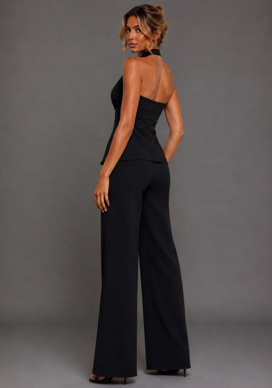 Side back image of a model wearing the VSPR Betty Tailored Longline Black Waistcoat with Elton Wide Leg Black Tailored Trousers, highlighting the elongated tailored silhouette against a grey studio backdrop