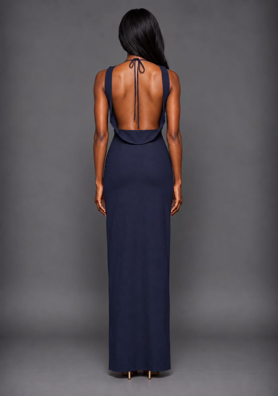 Back image of a model wearing the VSPR Brodi Backless High Neck Maxi Dress in Navy, showcasing the sophisticated open-back detail and streamlined fit against a grey studio backdrop
