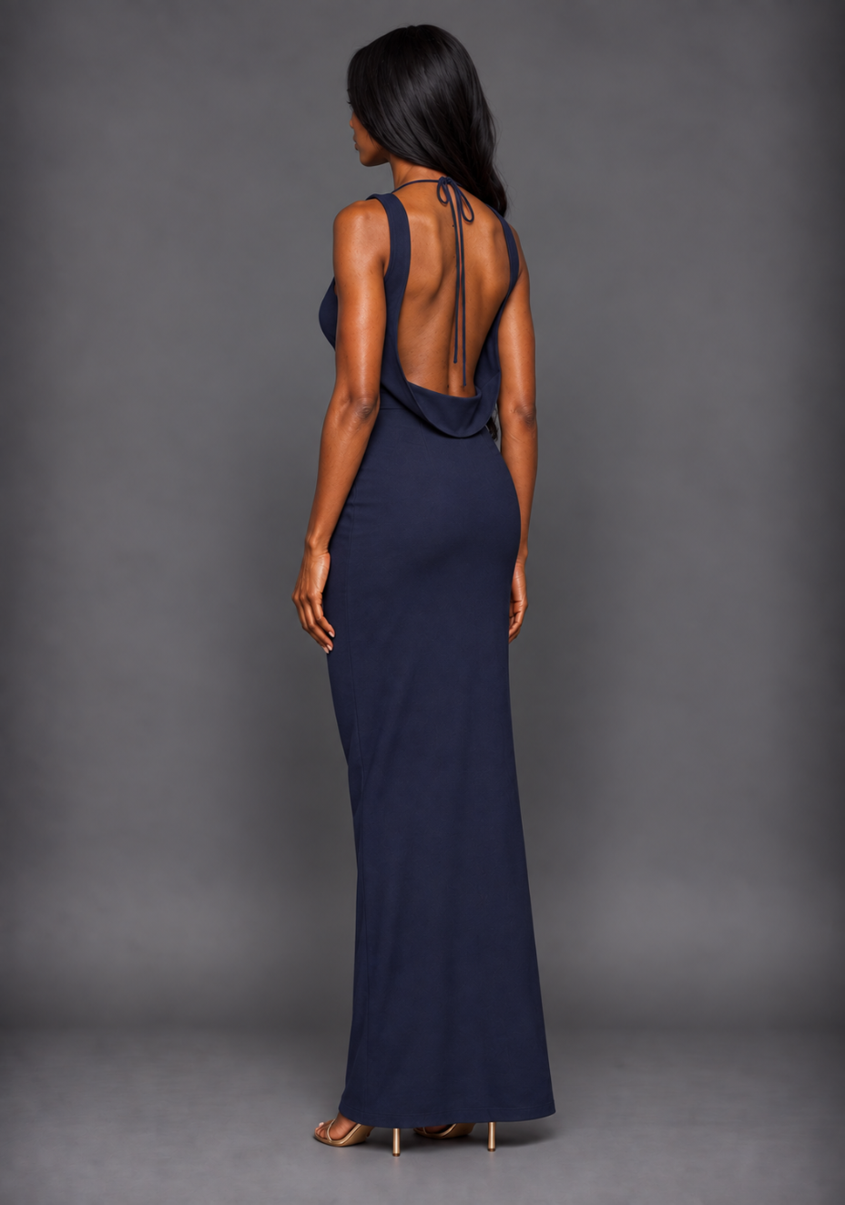 Side back image of a model wearing the VSPR Brodi Backless High Neck Maxi Dress from a side back angle, showcasing the exposed back and sleek body-skimming fit against a grey studio backdrop.