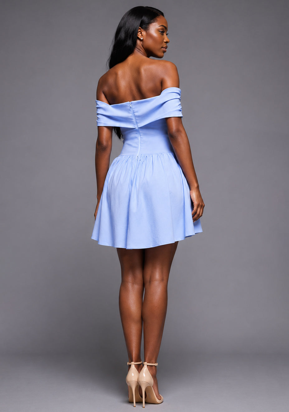 Back image of a model wearing the VSPR Carla Bardot Foldover Blue Mini Dress in Light Blue with a clean off-the-shoulder neckline, tailored body-skimming fit, and contemporary mini-length hem, standing against a grey studio backdrop.