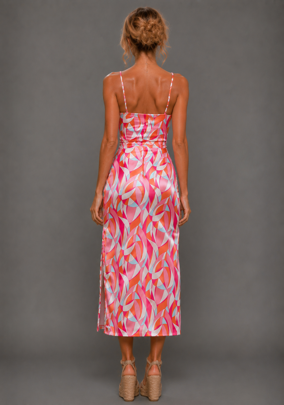 Back image of a model wearing the VSPR Harper Geo Print Satin Midaxi Dress showcasing its sleek midaxi silhouette, slim shoulder straps, gathered waist, and vibrant geometric satin print against a grey studio backdrop