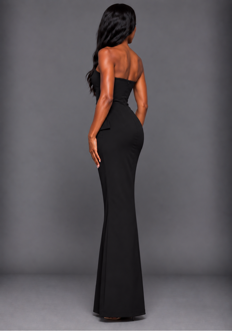 Side-back image of a model wearing the VSPR Isabel Bandeau Ruched Waist Detail Black Maxi Dress, showcasing the smooth black fabric and contoured fit through the waist and hips.