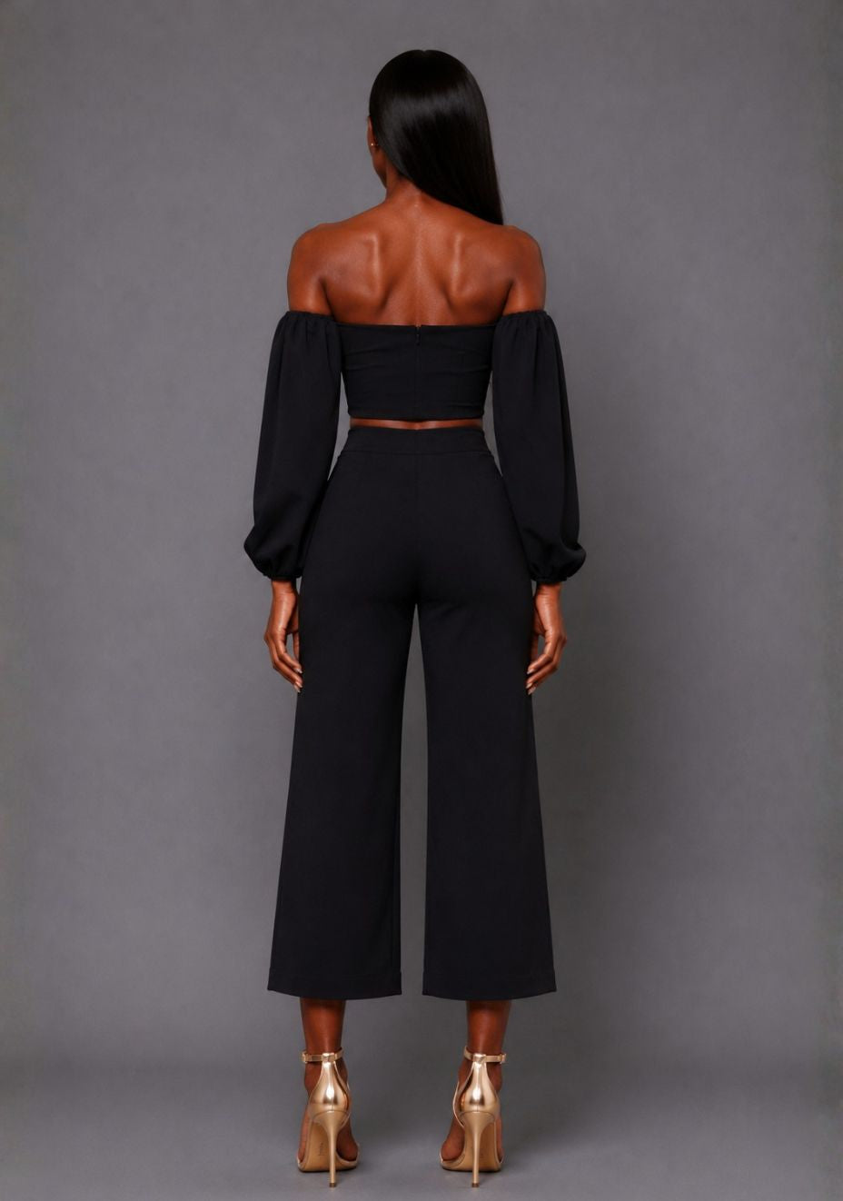 Back image of a model wearing the VSPR Mindi Wide Leg Black Cropped Trousers, showcasing the sleek high-rise waist and elegant wide-leg silhouette against a grey studio backdrop