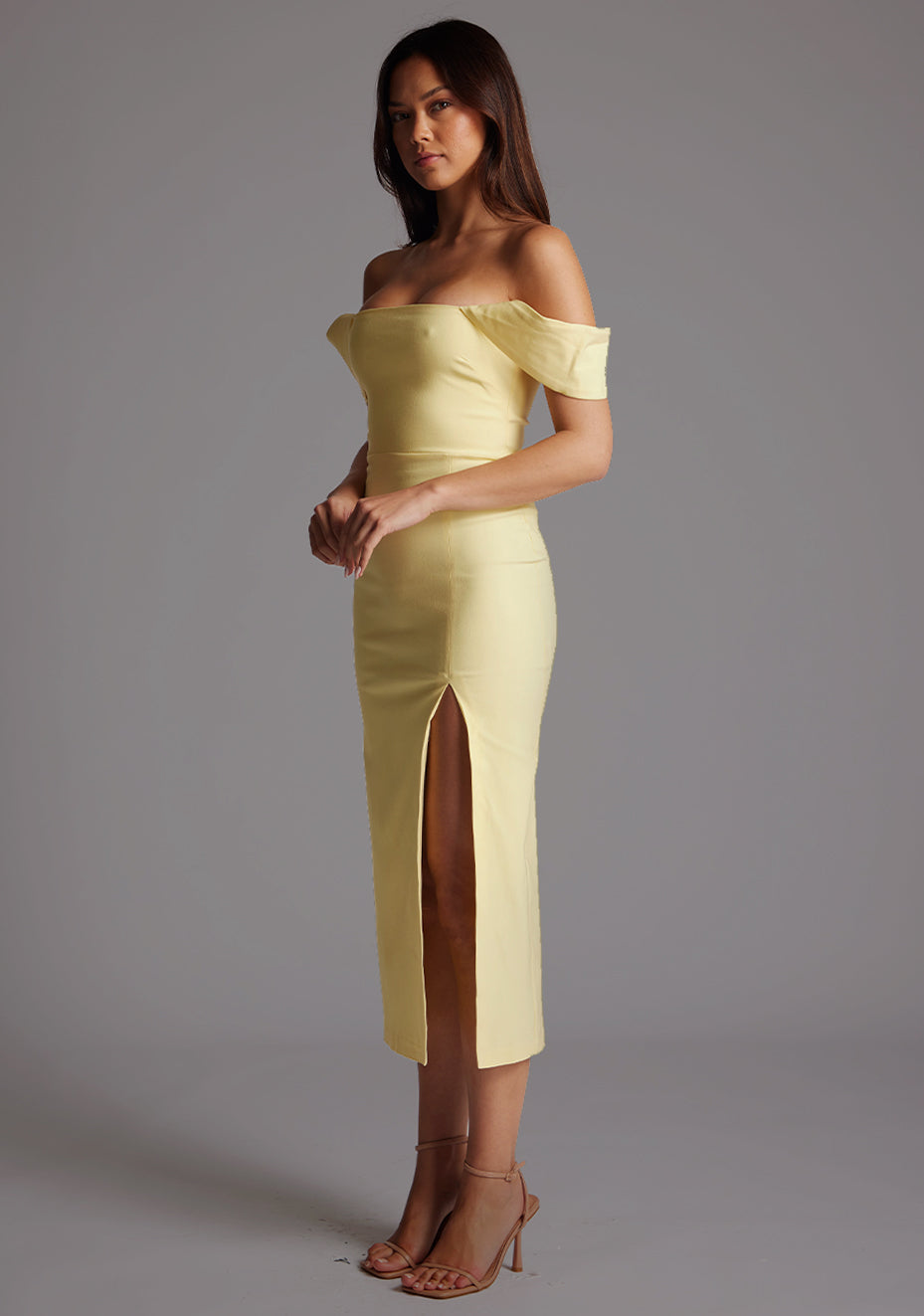 Side front image of a model wearing the VSPR Astra Bardot Lemon Midaxi Dress, showcasing the fitted silhouette, Bardot neckline, and front thigh split against a grey studio backdrop.
