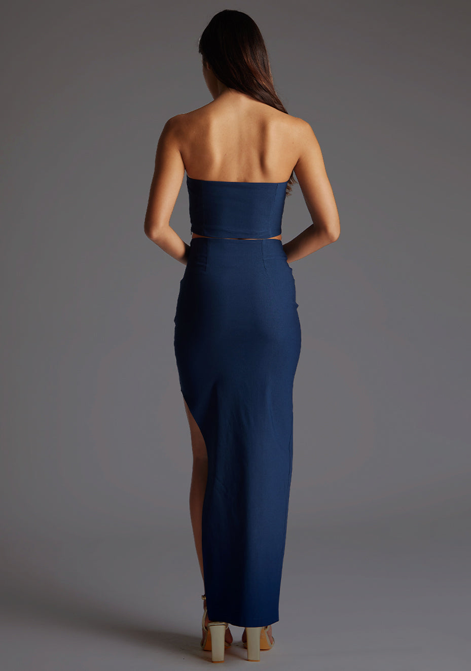 Back image of a model wearing the Vesper Benedetta Strapless Crop Top in Navy, displaying the clean strapless back and smooth, body-skimming fit against a grey studio backdrop.