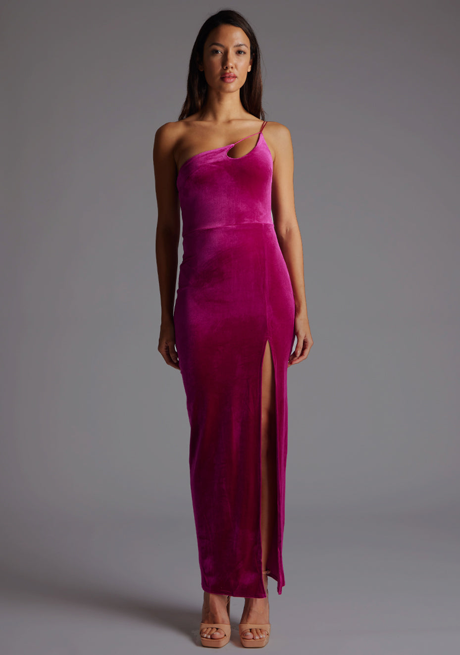 Front image of a model wearing a magenta maxi dress with a flattering asymmetric cut-out neckline, finished with a one shoulder strappy detail and front skirt split. The design featured is the Vesper Daniella One Shoulder Velvet Maxi Dress Magenta.