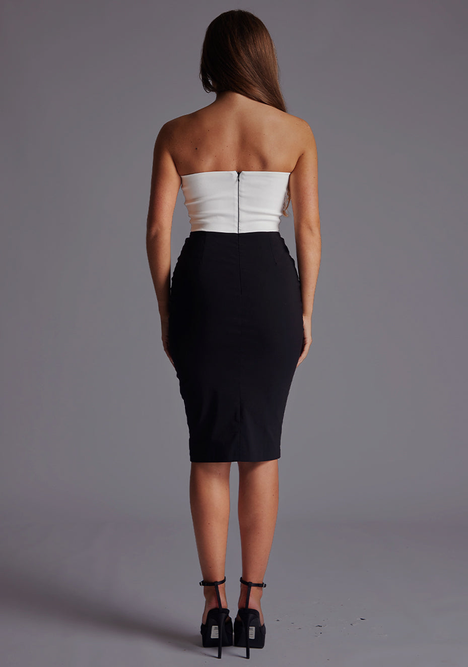 Back image of a model wearing a monochrome midi dress with a stunning strapless and the back zipper ensures a comfortable fit. The design featured is the Vesper Drew Strapless Midi Dress in Monochrome.