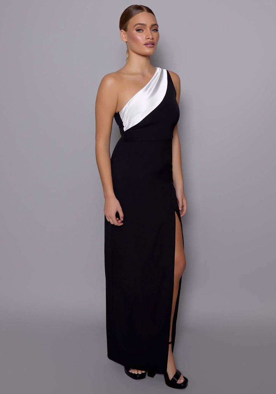 Side‑front view of the VSPR Fliss monochrome maxi dress showing the curve‑skimming silhouette, asymmetric shoulder line, and dramatic thigh‑high split for elegant movement.
