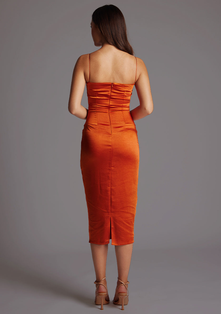 Back image of a model wearing a rust satin dress with a timeless sweetheart neckline, delicate thin straps, and a convenient back zip. The design featured is the Vesper Hibiscus Ruched Bust Satin Midaxi Dress in Rust.