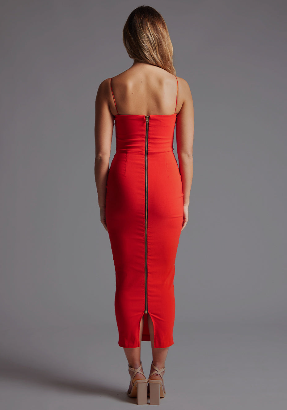 Back image of a blonde model wearing a Red Midaxi Dress with a halter neckline, thin straps, and a front bodice cut-out, the design features the  Vesper Jordan Cut-Out Midaxi Dress in Red.
