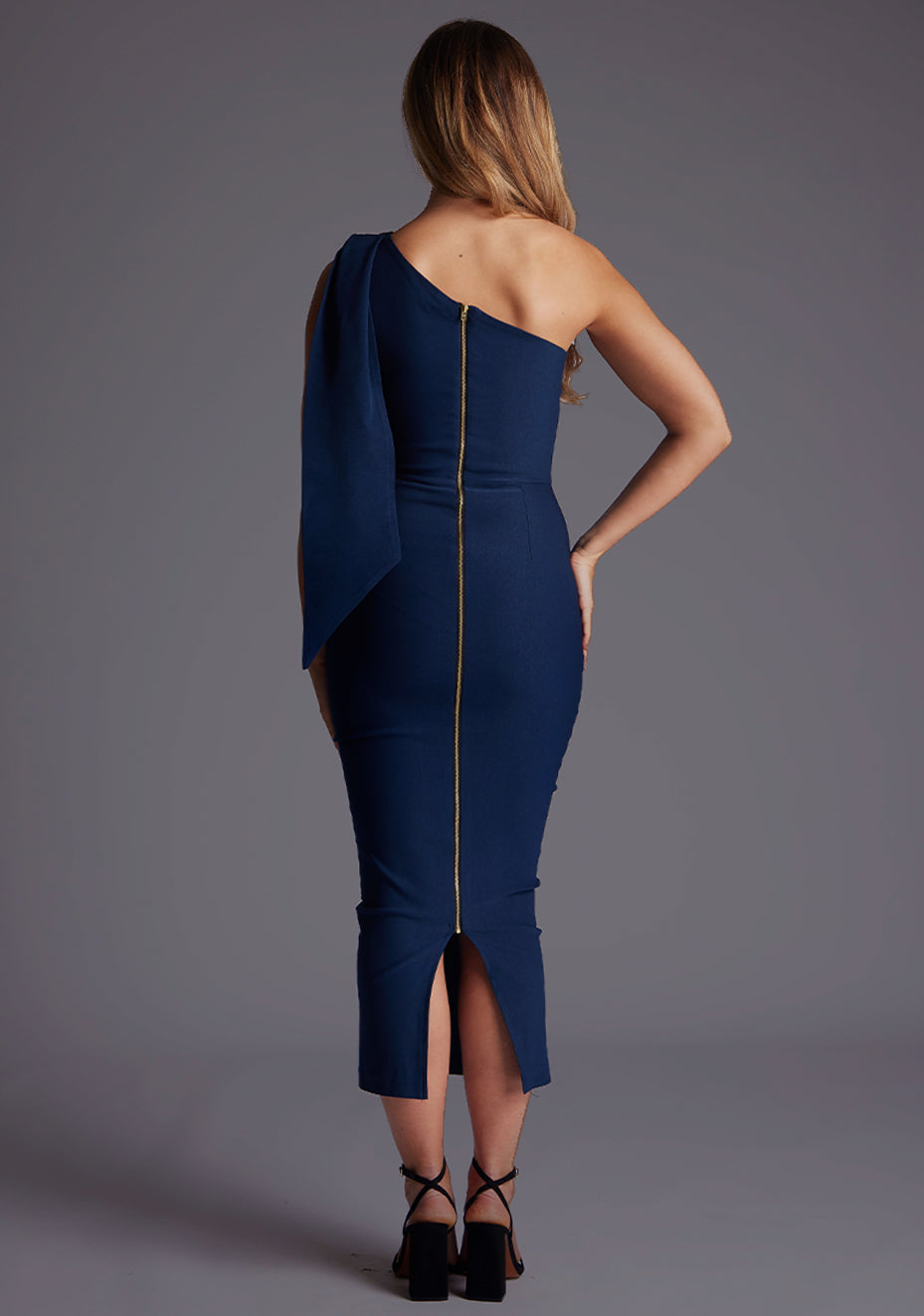 Back image of a model wearing a navy midaxi dress with a chic one-shoulder design and an asymmetric silhouette, it effortlessly captivates with its modern flair. The design featured is the  Vesper Katrina One Shoulder Drape Midaxi Dress in Navy.