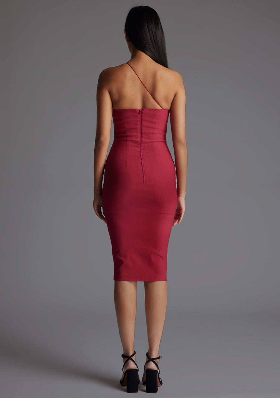 Back image of the model wearing an raspberry one shoulder midi dress with a asymmetrical neckline with one strap, bodycon silhouette and discreet back zip for seamless fit. The design featured is the Vesper Leslie One Shoulder Midi Dress in Raspberry.