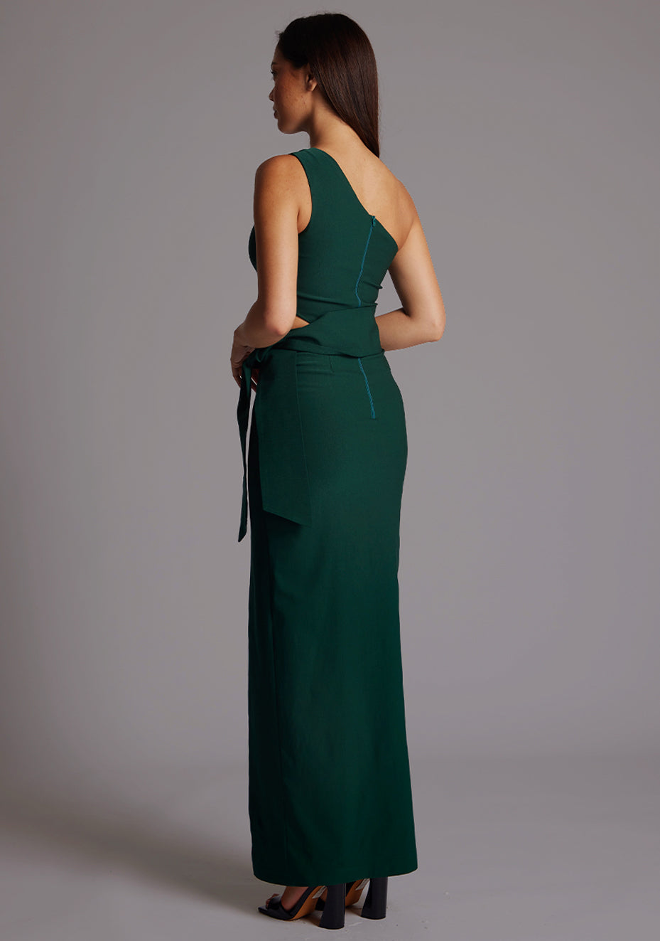 Side back image of a model wearing the Vesper Lisbeth One Shoulder Maxi Dress in Forest Green, highlighting the smooth back silhouette and fluid fabric fall.