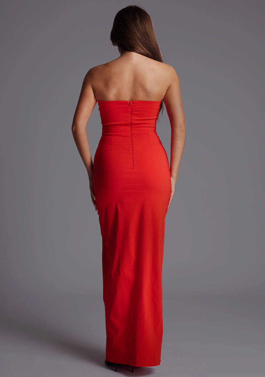 Back image of a model wearing the Vesper Salma Bandeau Thigh Split Maxi Dress in Red, displaying the minimalist strapless back and fitted maxi silhouette.