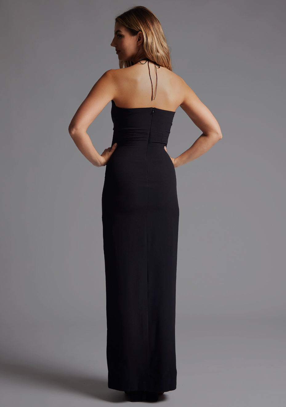 Side back image of a model wearing the Vesper Tanya Black Maxi Dress on a model, showcasing the clean halter cut and fluid movement of the fabric.