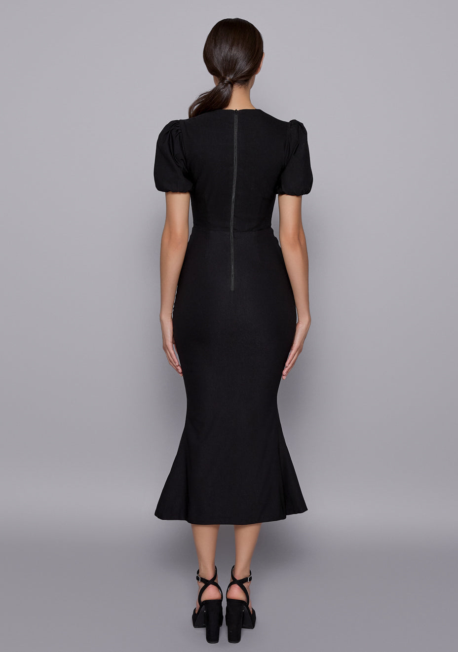 Back view of the VSPR Viola Dress in Black showing a tailored fit, zip closure, and gentle flare of the fishtail hem, complemented by structured puff sleeves.