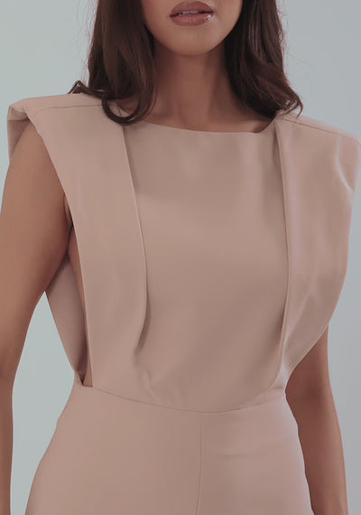 A model wearing the VSPR Bronte Open Back Jumpsuit in Stone, walking and posing in a gray studio. The jumpsuit features structured shoulders, a sculpted bodice, an open back, and wide-leg trousers. The model turns to show the open-back detail and moves gracefully to highlight the flow and fit of the fabric.